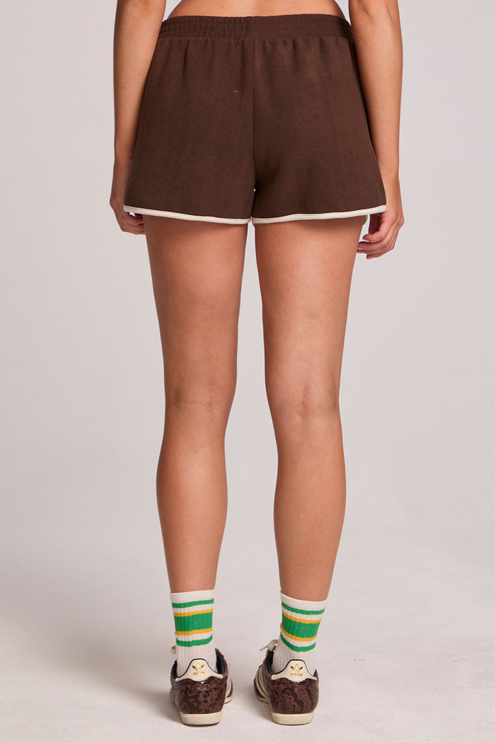 Back view of a woman wearing them Chaser Eyla Worn Brown Shorts  and matching brown sneakers on a neutral background