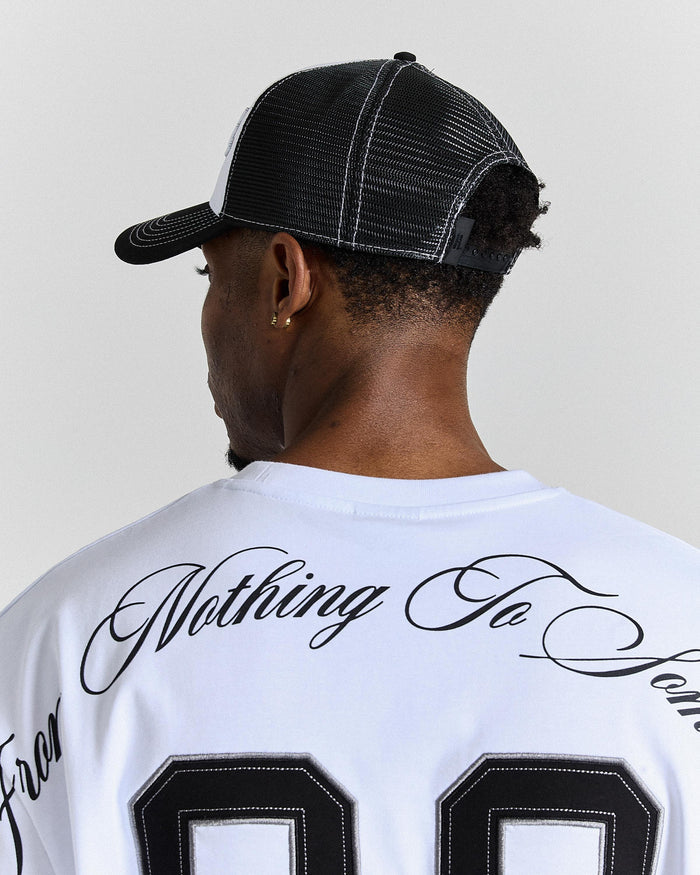 Person wearing a white t-shirt with black text and a black cap on a plain background