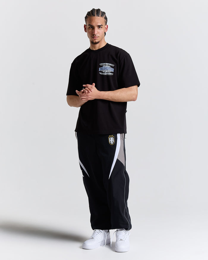 Man wearing a black t-shirt and black pants with white accents on a light gray background