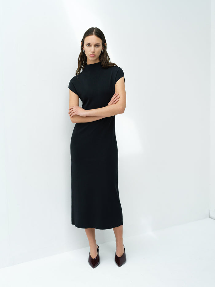 A woman wearing a dark grey knit bodycon midi dress with a high neck and short sleeves.