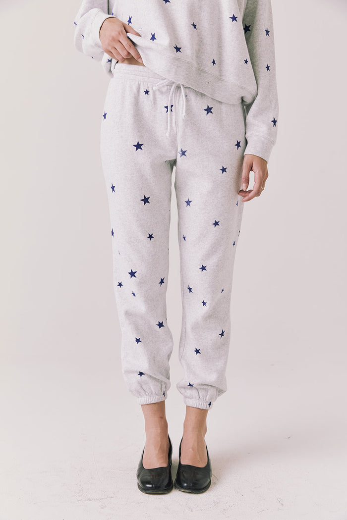 Full body view of woman wearing Chaser’s Festive Stars Joggers in light grey with star patterns and matching top on a white background