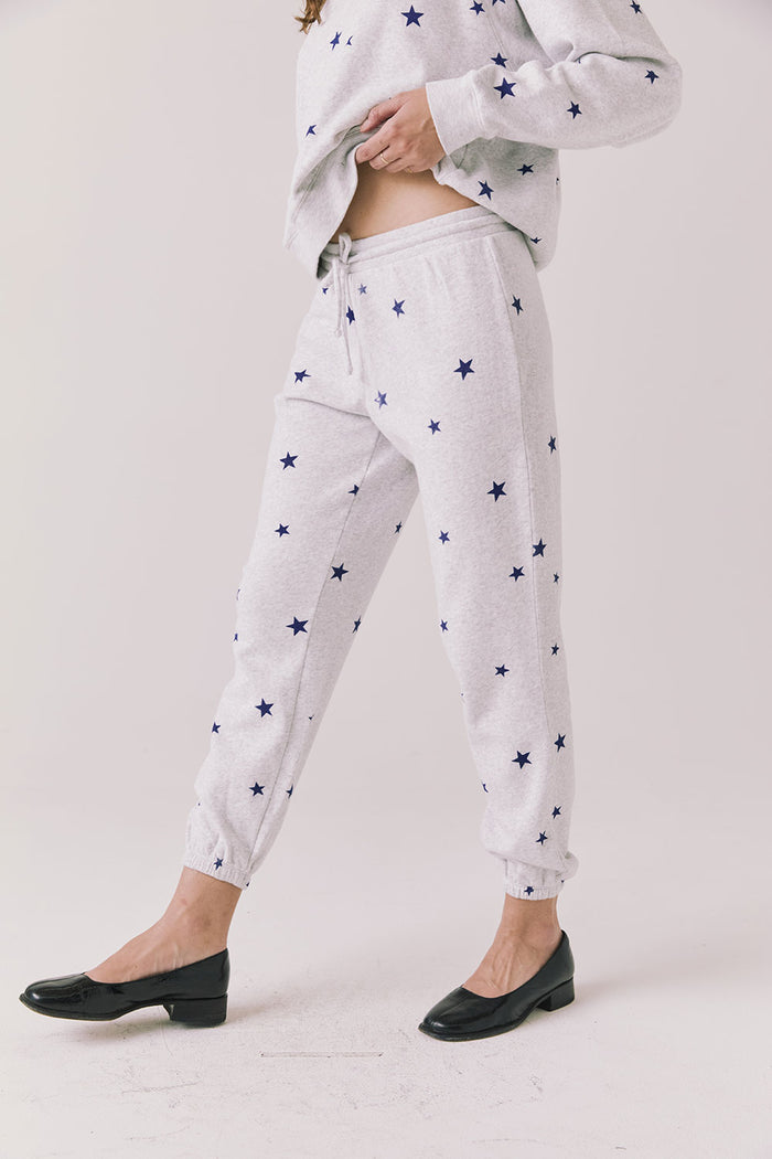 Side view of woman wearing Chaser’s Festive Stars Joggers in light grey with star patterns on a white background
