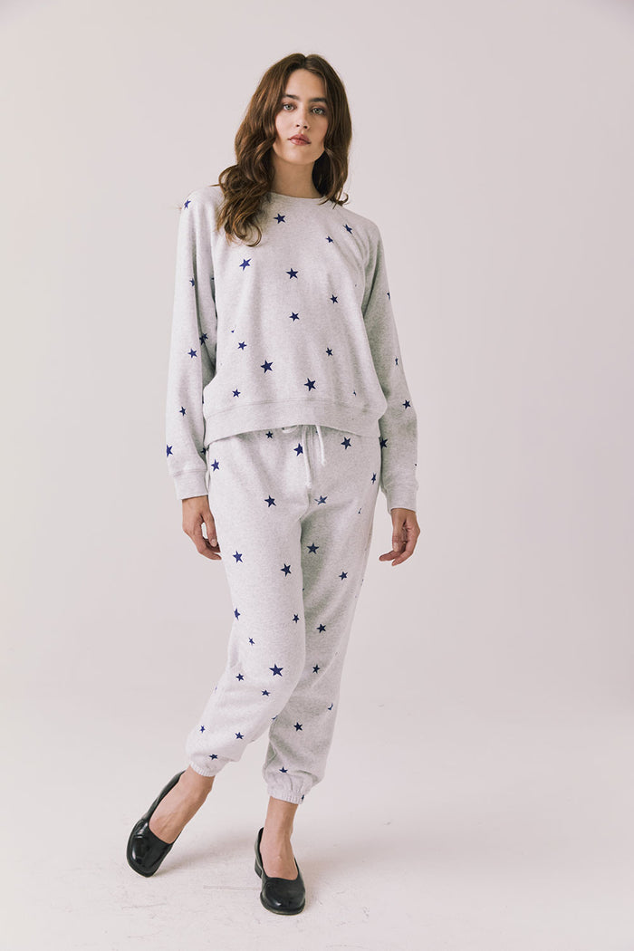 Full body view of woman wearing Chaser’s Festive Stars Pullover in Light Grey with star patterns and matching Festive Stars Joggers on a white background