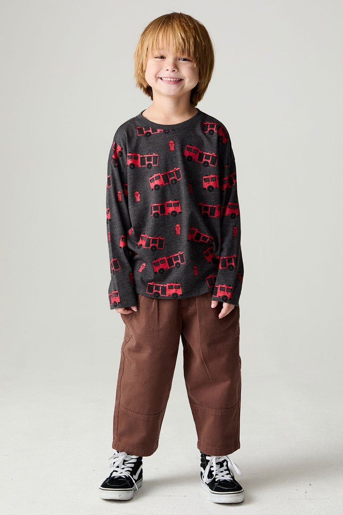 A full body front view of a boy wearing the Chaser Fire Trucks Boys Tee on a neutral background with brown pants