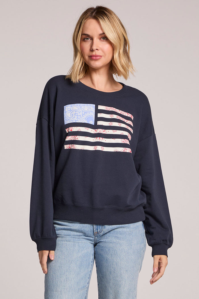 Front view of a woman wearing the Chaser Flag Adornment Long Sleeve and jeans on a neutral background