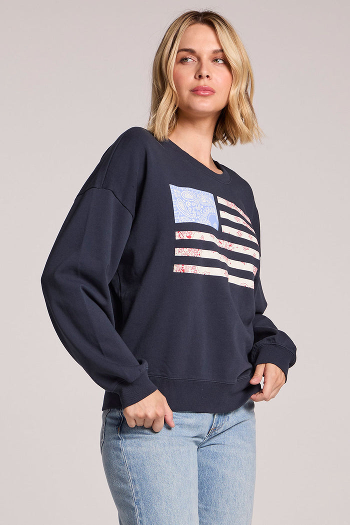 Side angle view of a woman wearing the Chaser Flag Adornment Long Sleeve on a neutral background with one hand in her pocket