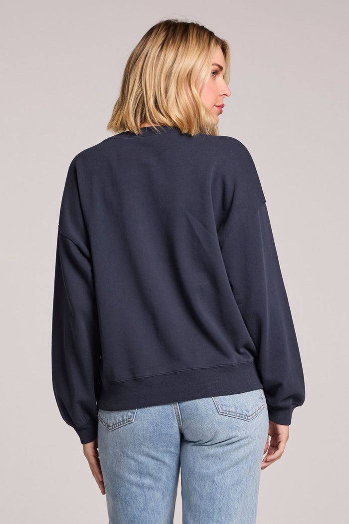 Back view of a woman wearing the Chaser Flag Adornment Long Sleeve on a neutral background looking over one shoulder