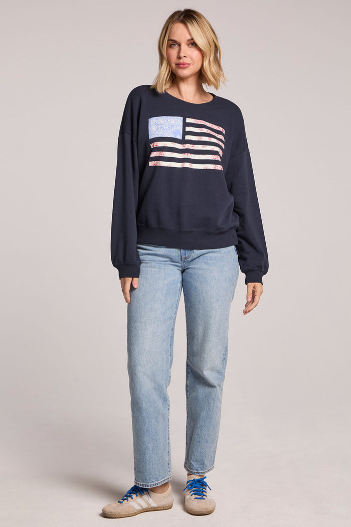 Full body front view of a woman wearing the Chaser Flag Adornment Long Sleeve and sneakers on a neutral background