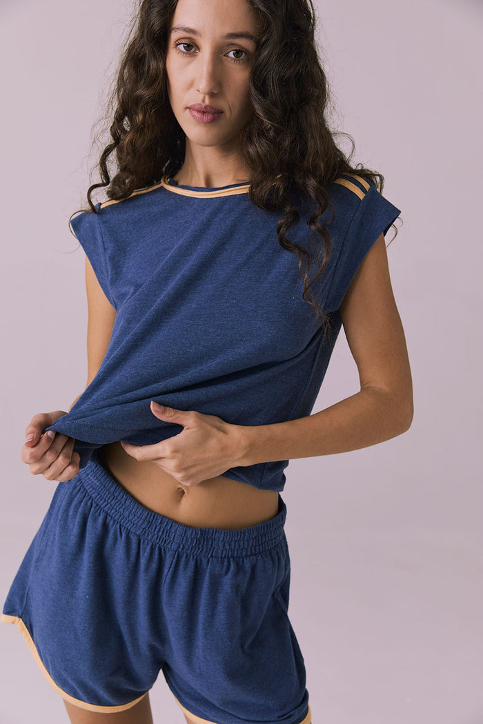 Studio image of the Chaser Flora Cropped Honest Indigo Cap Sleeve Crewneck Tee lightly lifted at the hem revealing soft elastic waistband on matching Taylorr Shorts