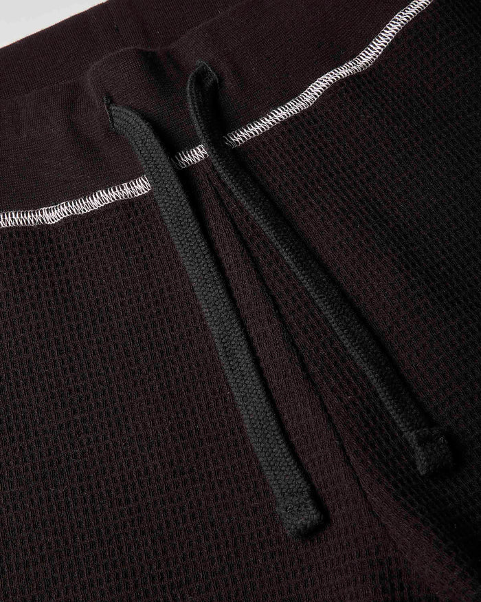Close-up detail of a dark brown waffle-knit garment, showing a black drawstring and white contrast stitching.