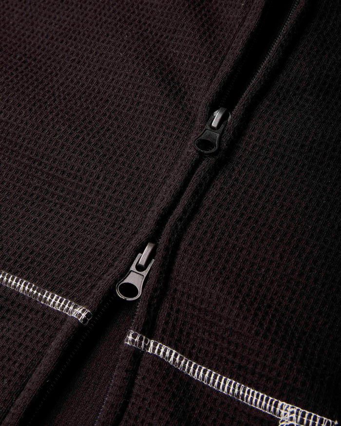 Close-up of a dark brown waffle-knit zippered garment, showing the textured fabric and silver-toned zipper pulls.