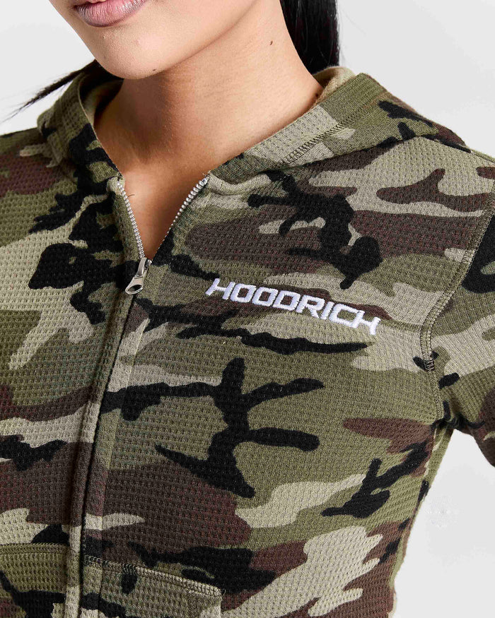 Close-up of a woman wearing a camouflage zip-up hoodie with the brand name 'HOODRICH' printed in white on the chest.
