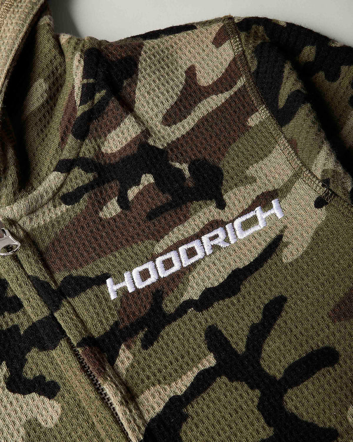 Close-up of a camouflage mesh zip jacket with a white embroidered 'HOODRICH' logo on the chest.