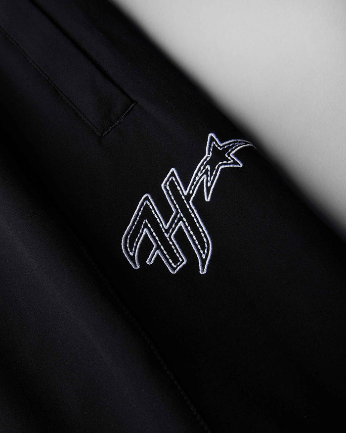 Close-up of a black garment featuring a white embroidered stylized monogram with a star on the chest.