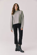 Full body view of woman wearing Chaser’s Frankie Heather Grey Pullover Sweater with black pants and black boots on a white background