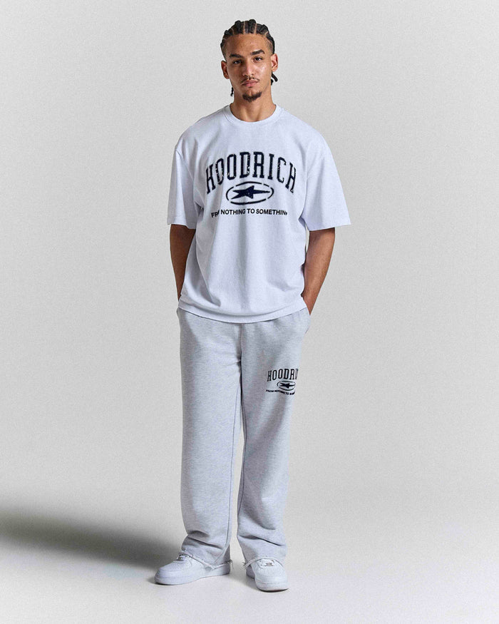 Front view of a male model wearing a regular-fit white Hoodrich t-shirt with dark blue, distressed-effect varsity-style branding.