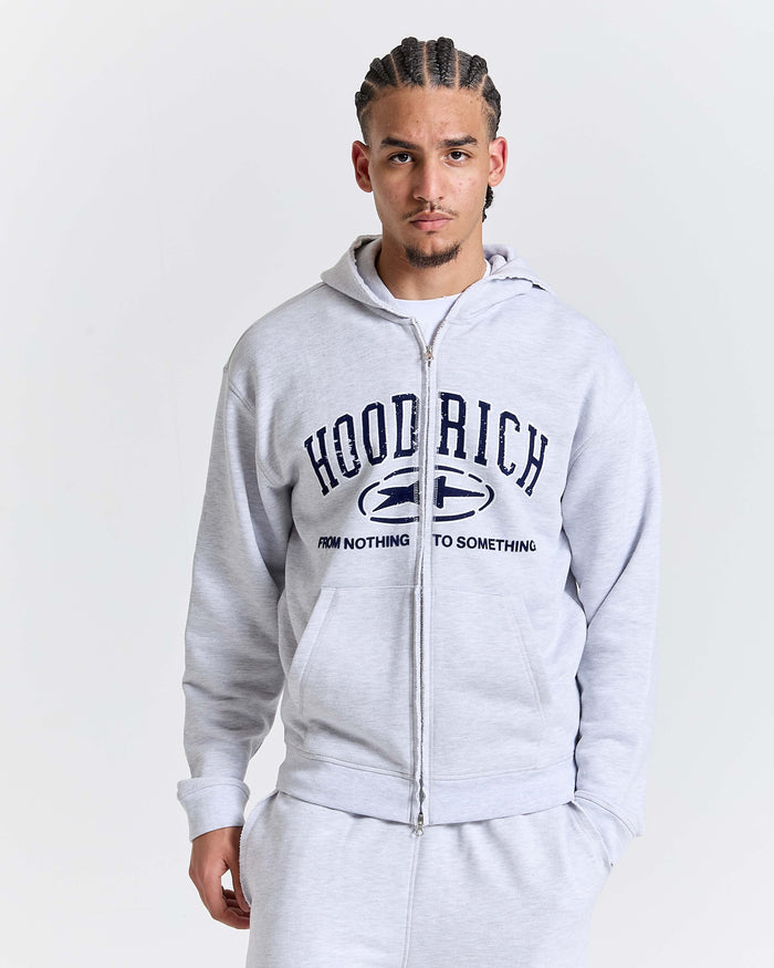 Male model wearing a relaxed grey marl zip-up hoodie with varsity-style Hoodrich branding and the slogan 'From Nothing To Something'