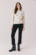 Full body view of woman wearing Chaser’s Starry White French Scripts Long Sleeve with French phrases like “Merci” and “Bonjour” in black text, black pants, and black boots on a white background
