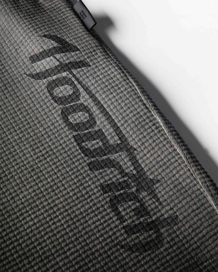 Close-up of a dark gray textured fabric surface with a large black diagonal 'hoodedog' logo and a small black brand tab near the top edge.