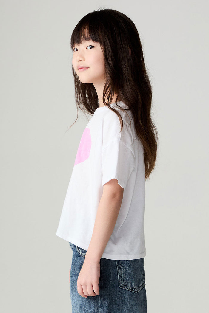 Side view of a girl wearing the Chaser Full Of Love Girls Tee on a neutral background with jeans and hands at sides