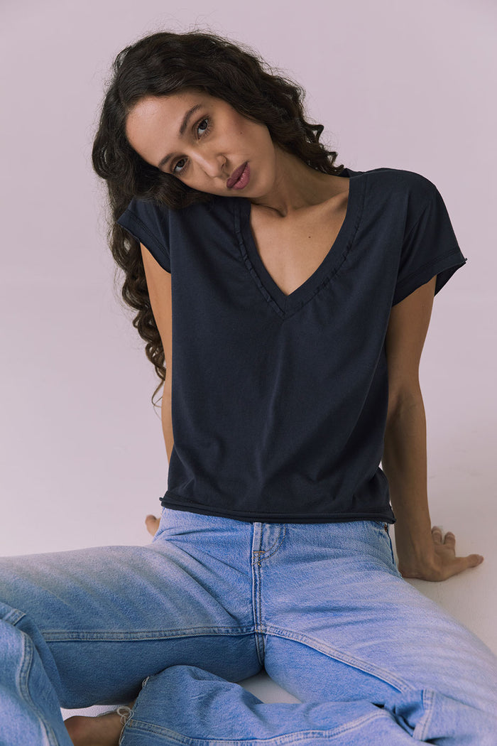 Studio image of the Chaser Gator V Neck Licorice Black Tee while seated in light-wash denim jeans capturing a relaxed effortless vibe