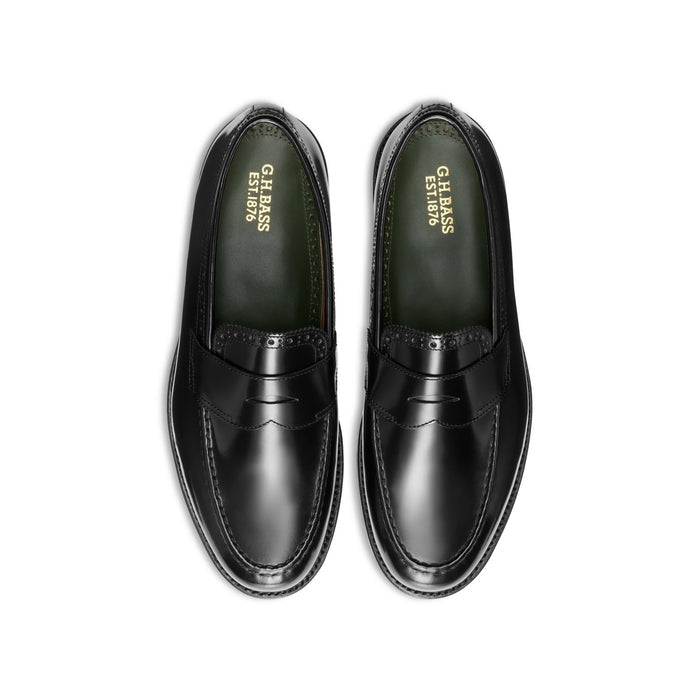 Black leather penny loafers with perforated brogue trim, top-down view showing green insoles.