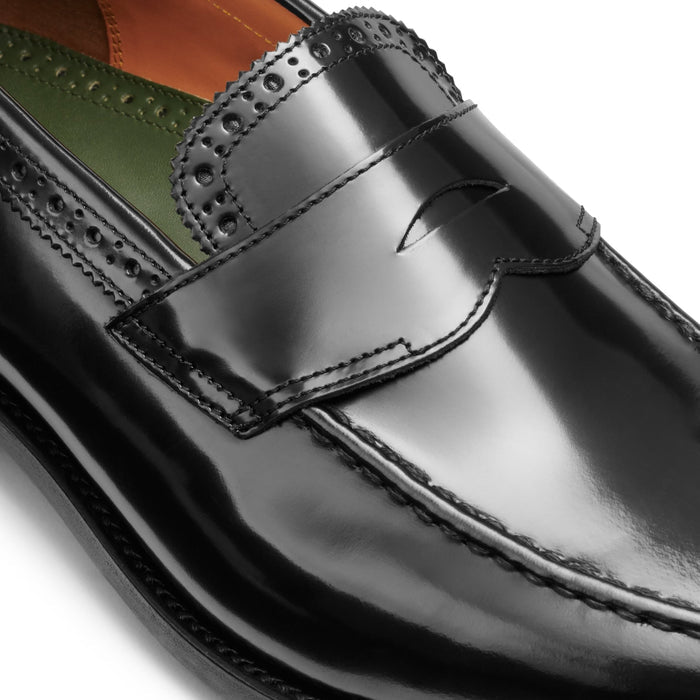 Close-up of a black leather loafer's penny strap and perforated brogue trim.