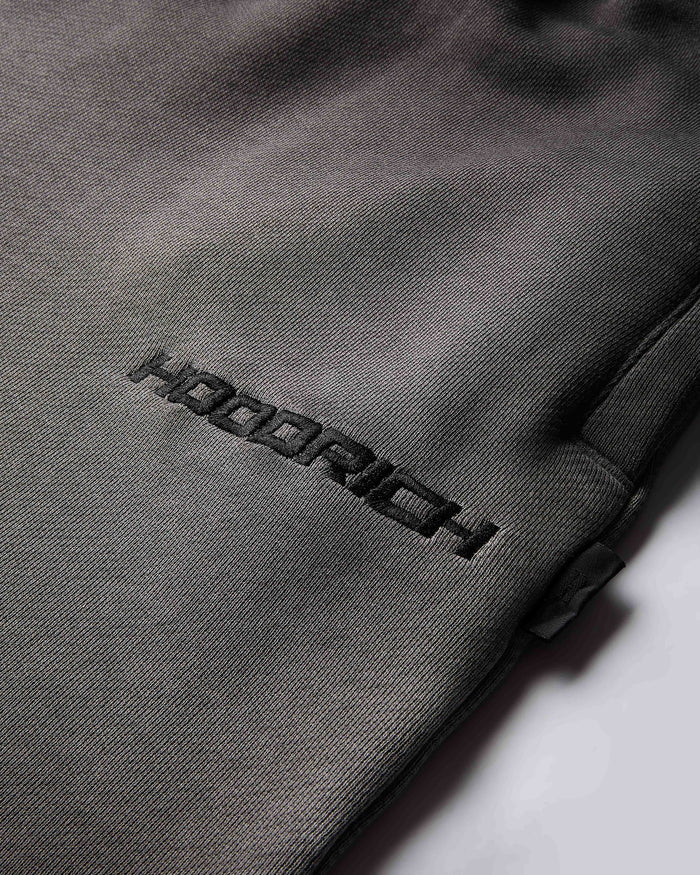 Close-up of the black Hoodrich logo embroidered on the black oil wash fabric of the shorts.