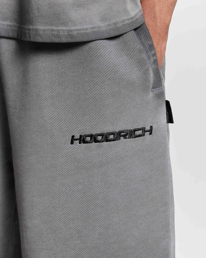 Close-up of the Hoodrich logo embroidered on a model wearing oversized black oil wash shorts.
