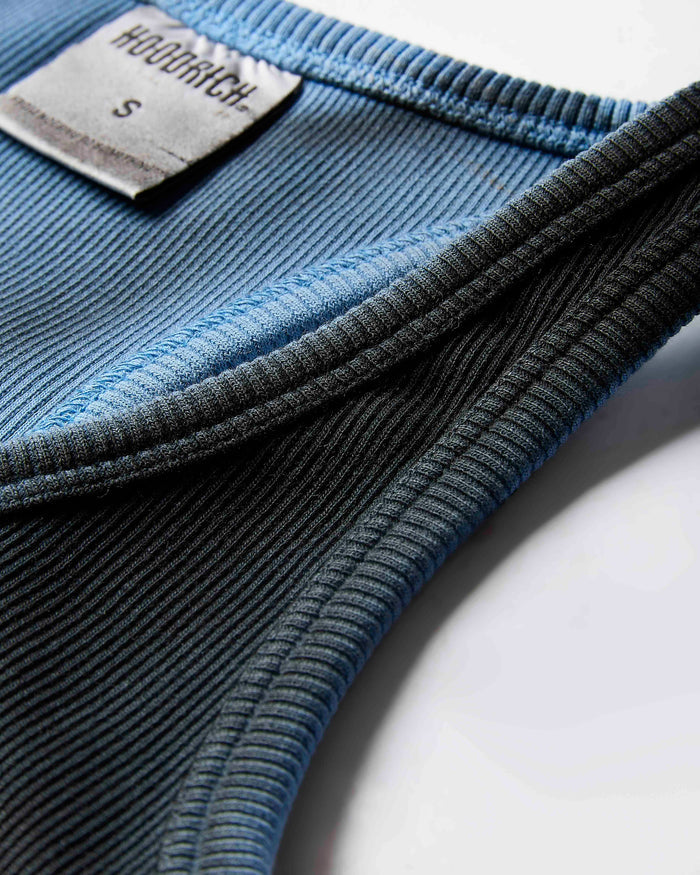 Close-up of the ribbed fabric and branded neck label on a black and blue ombre racer vest.