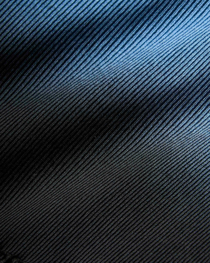 Extreme close-up of the black and blue ribbed fabric texture of the garment.