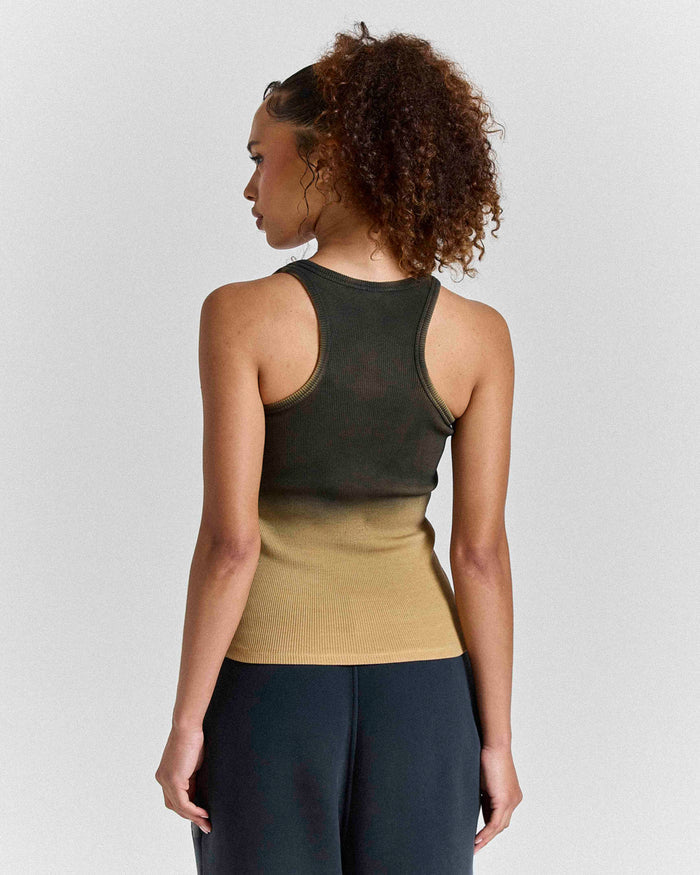 Person wearing a green tank top over a beige layer with black pants on a plain background