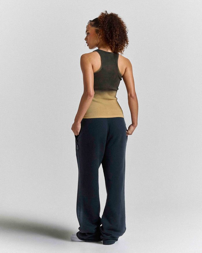 Woman wearing a green tank top and black pants against a plain background