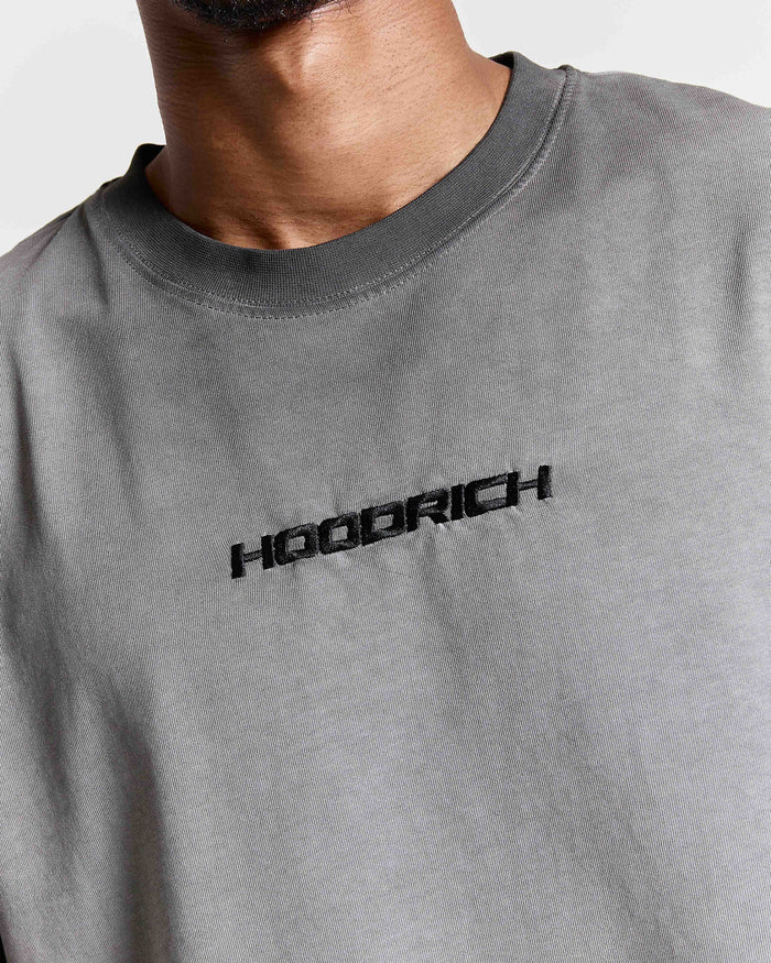 Close-up of the black embroidered Hoodrich logo on the chest of an oversized black oil wash t-shirt.