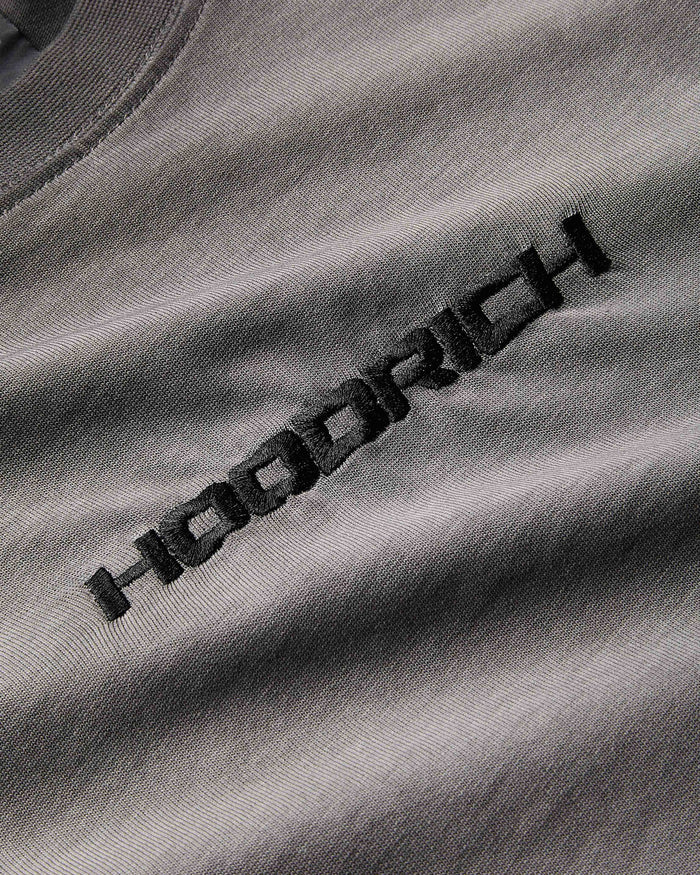 Extreme close-up of the black embroidered Hoodrich logo and textured fabric on an oil wash t-shirt.
