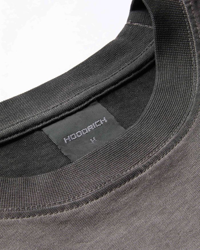 Close-up of the ribbed neckline and branded neck label on an oversized black oil wash t-shirt.