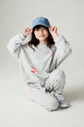 Girl crouching down wearing the Chaser irl Power Medley Girls Long Sleeve on a neutral background and matching pants and hat