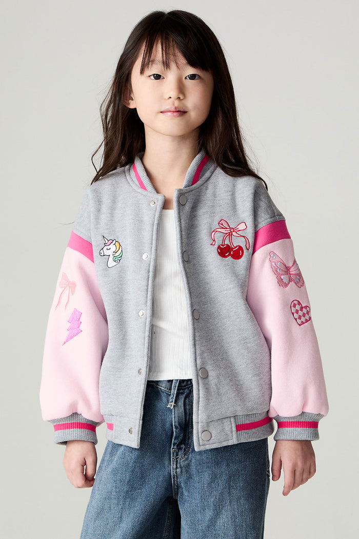 Front view of a girl wearing the Chaser Girl Power Medley Varsity Girls Varsity Jacket, white tee, and baggy jeans on a neutral background