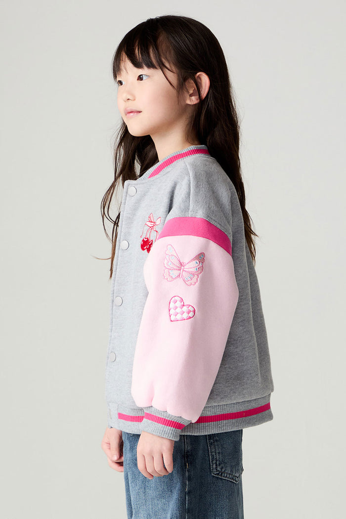 Side view of a girl wearing the Chaser Girl Power Medley Varsity Girls Varsity Jacket and baggy jeans on a neutral background