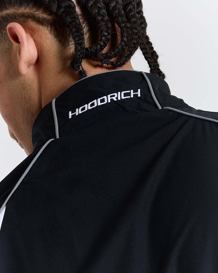 Person wearing a black jacket with 'HOODRICH' branding on the back against a light gray background