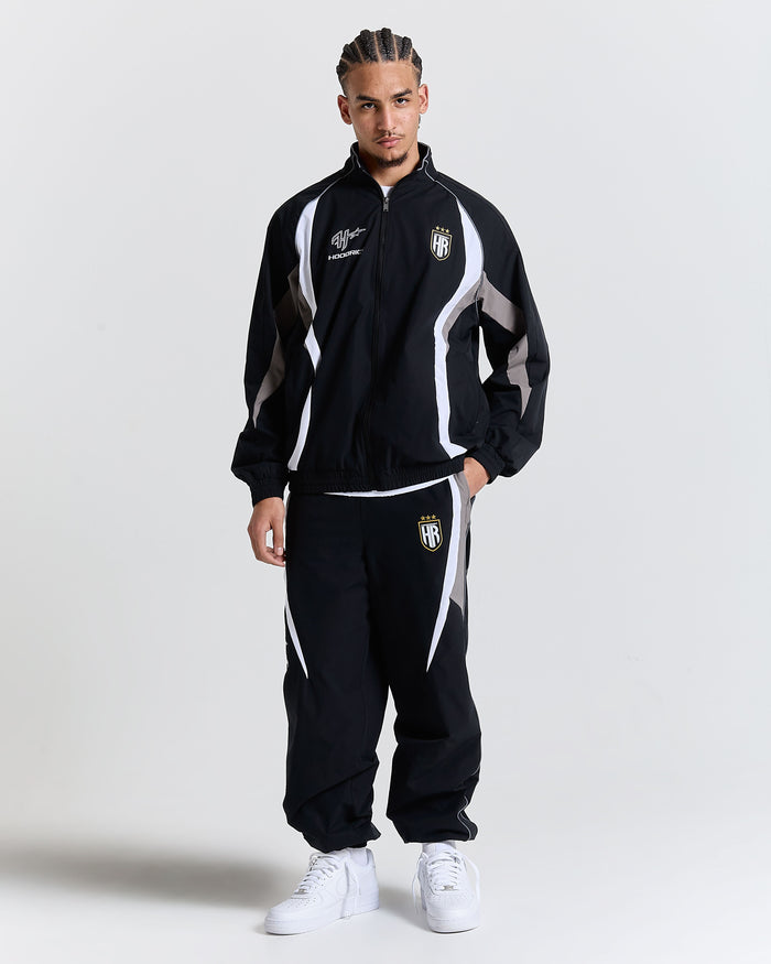 Person wearing a black tracksuit with white accents on a plain background