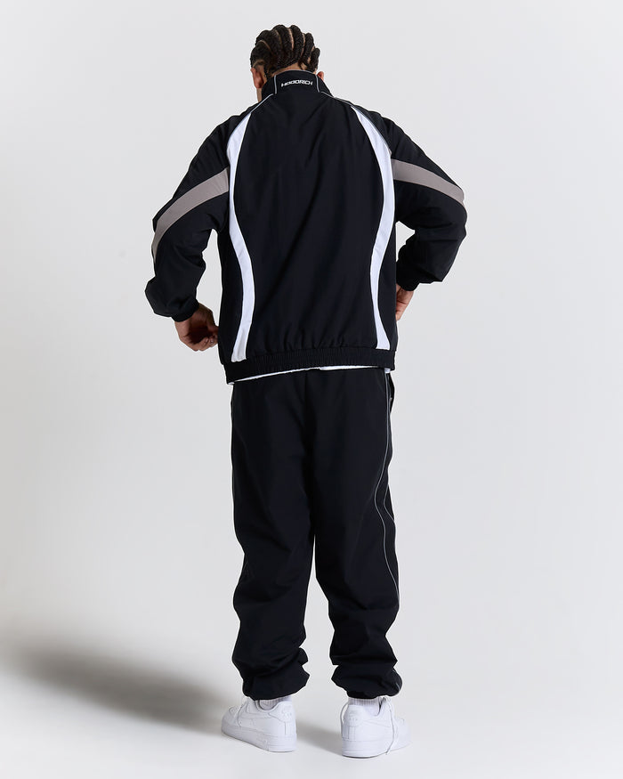 Person wearing a black tracksuit with white and gray stripes on a light gray background