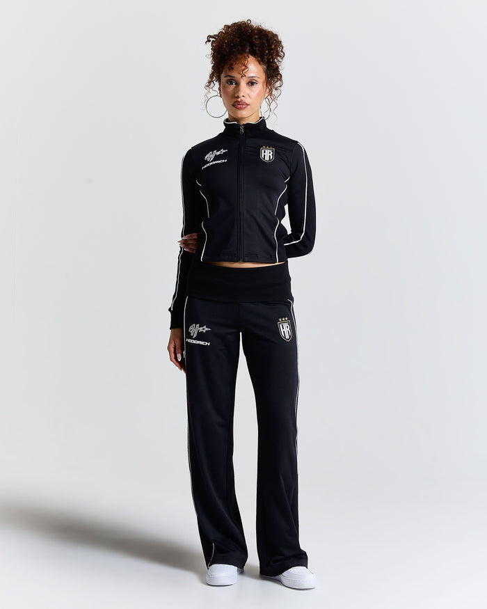 Woman wearing a black tracksuit with logos on a light gray background