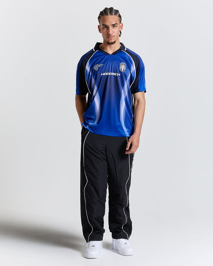 Person wearing a blue sports jersey with black accents and black pants on a white background