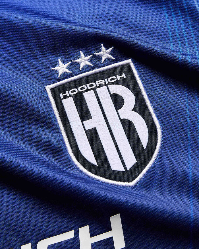 Close-up of a blue fabric with a logo featuring 'Hoodrich' and 'HB'.