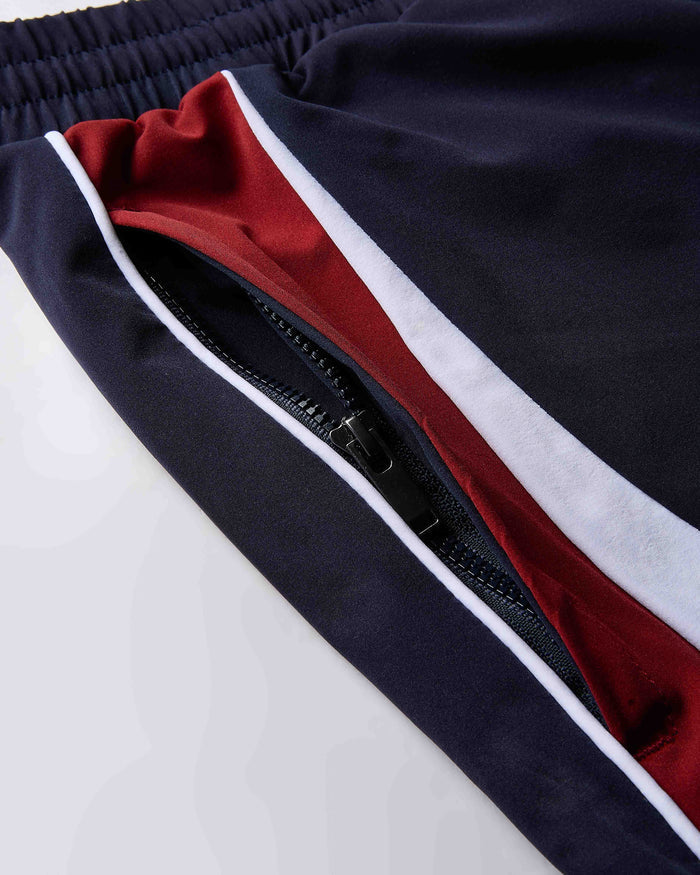 Close-up of a navy blue and red track pants with a zipper on a light gray background