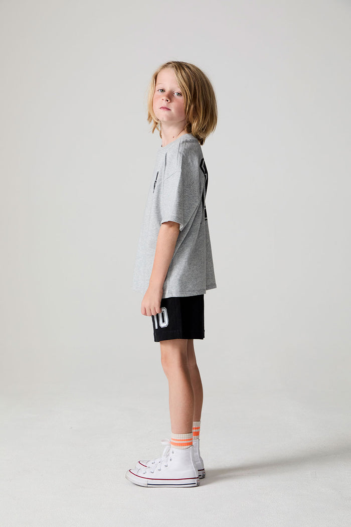 Full body side view of a boy wearing the Chaser Go Team Tee  on a neutral background