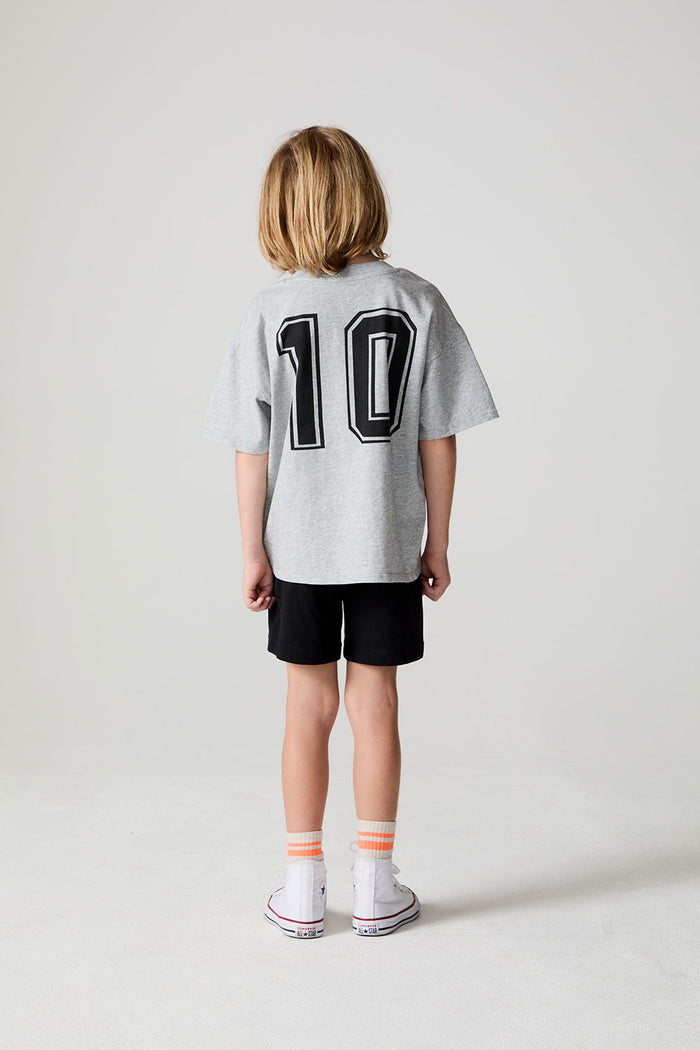 A full body back view of a boy wearing the Chaser Go Team Tee  on a neutral background