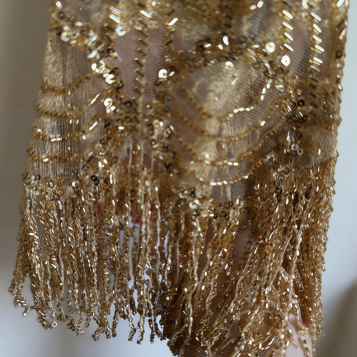Gold beaded bridal capelet with hand embroidered sequins and flowing fringe on illusion mesh for luxury weddings.
