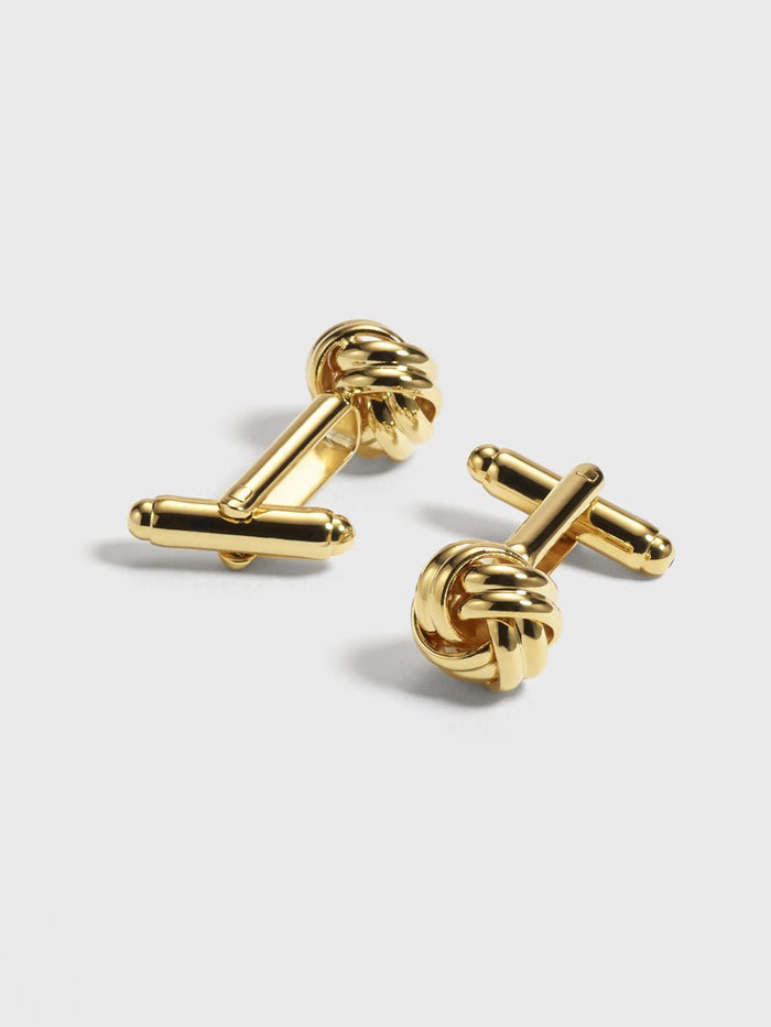 Gold cufflinks with a twisted knot design on a light background.